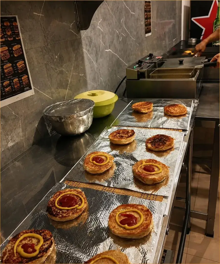 Pães de hambúrguer tostados enfileirados na bancada da cozinha da Royal Straight Burger, alguns já com ketchup e mostarda